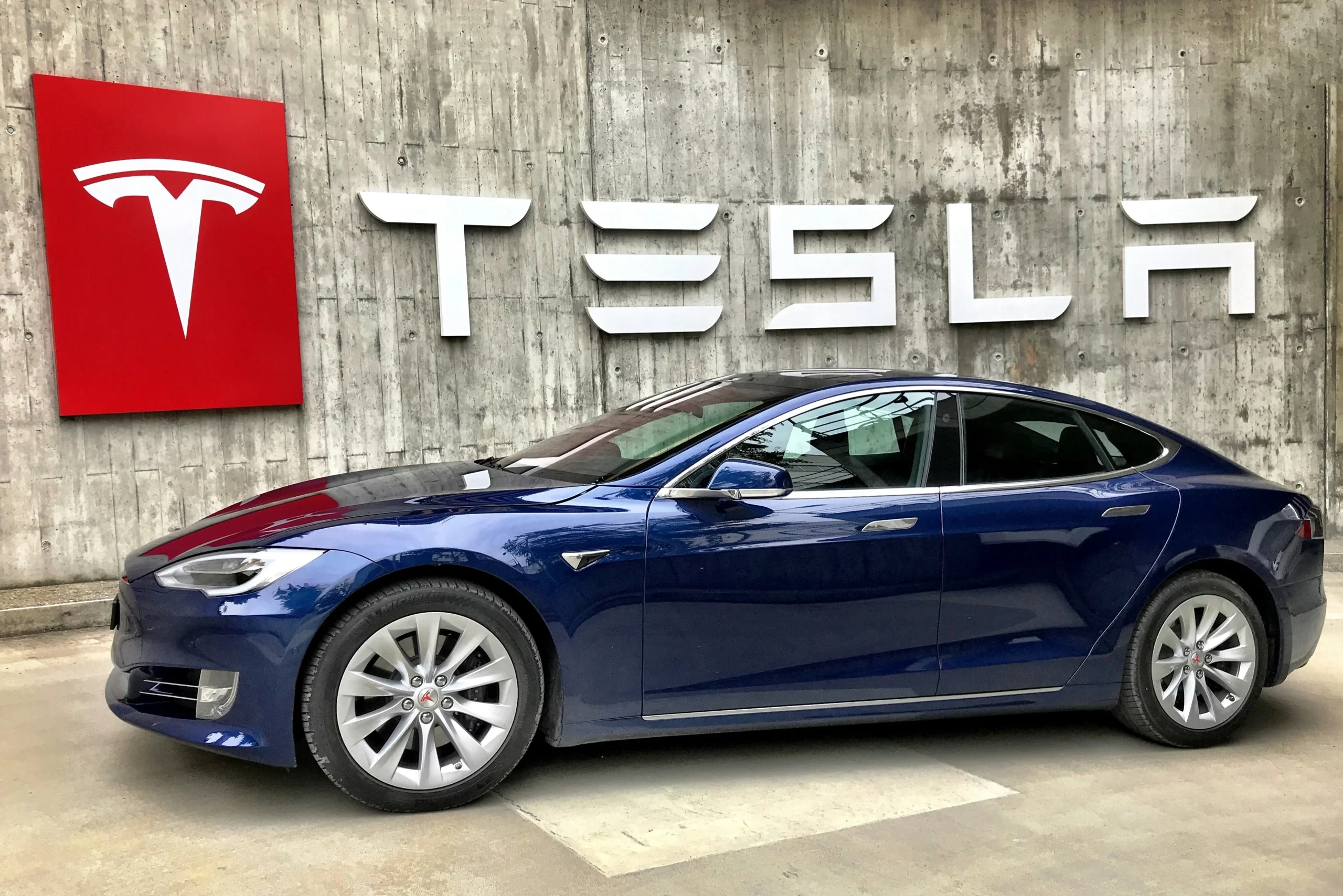 A sleek, blue Tesla car parked in a showroom, representing Elon Musk's innovative and environmentally-friendly personal brand image.